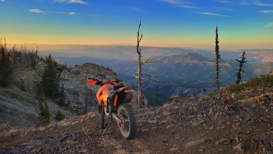 motorcycle parked on a ridge with hills behind it at sunset