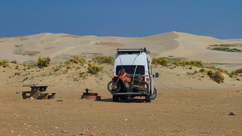 A van with sand dunes behind it 