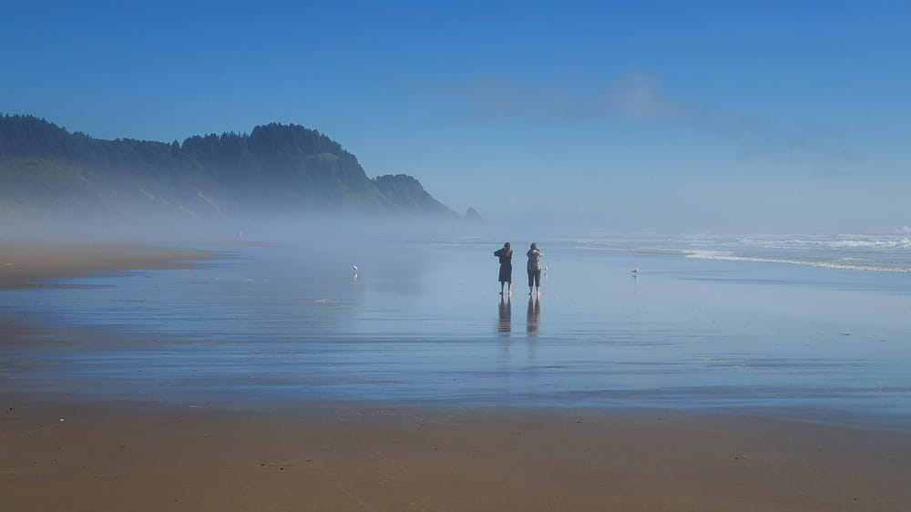 two people walking on a beach with fog off the coast