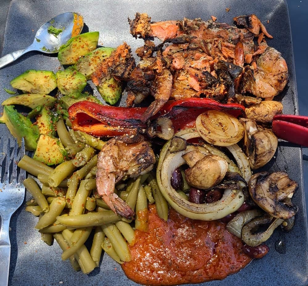 a plate of grilled veggetables, shrimp and sauce on the side