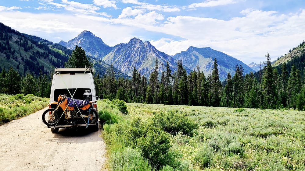 van parked on a dirt road with jagged mountains behind