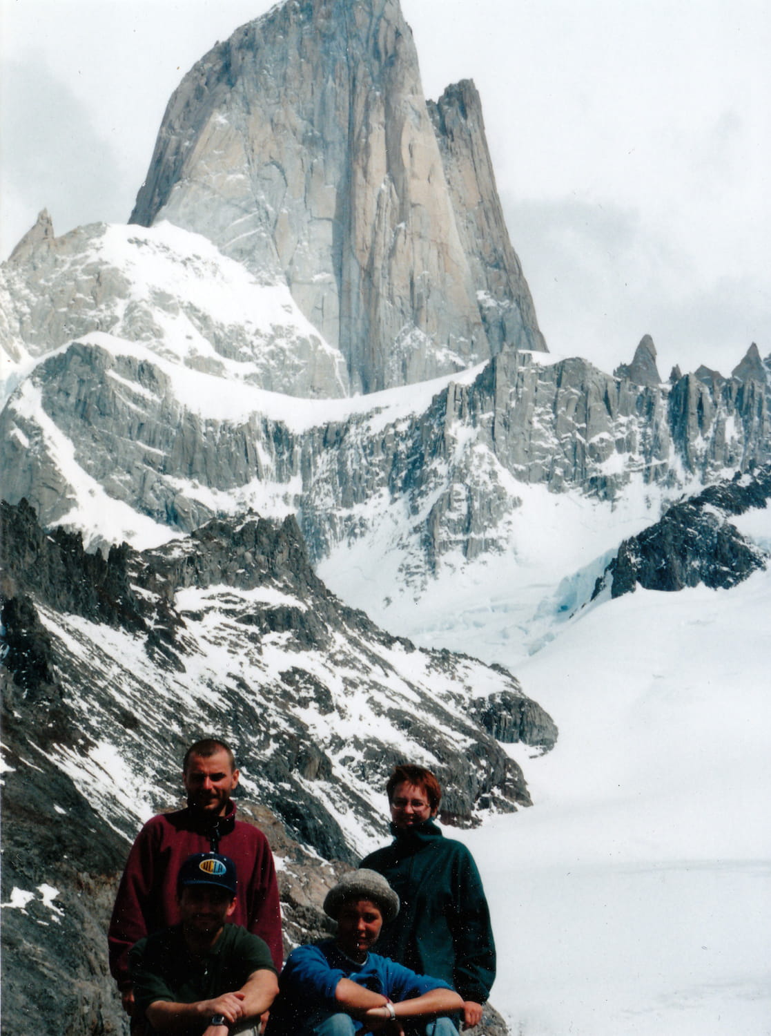 three people with glacier covered rock monolith behind 