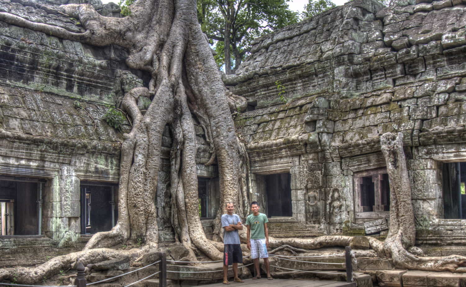 two people next to a tree growing around a rock temple