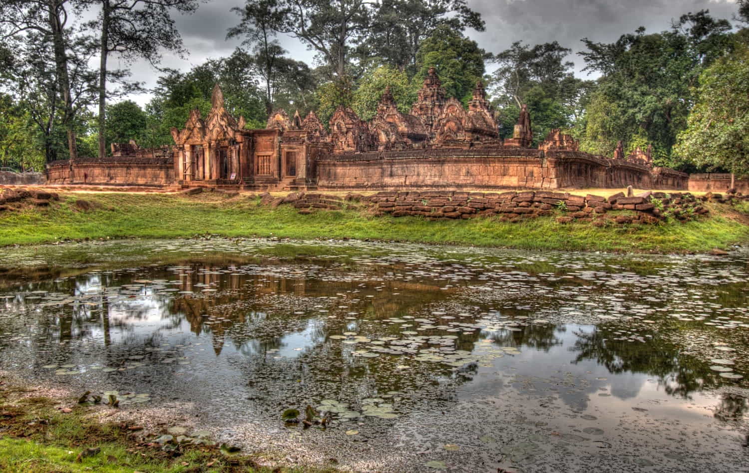 a pond with ruins of a temple behind