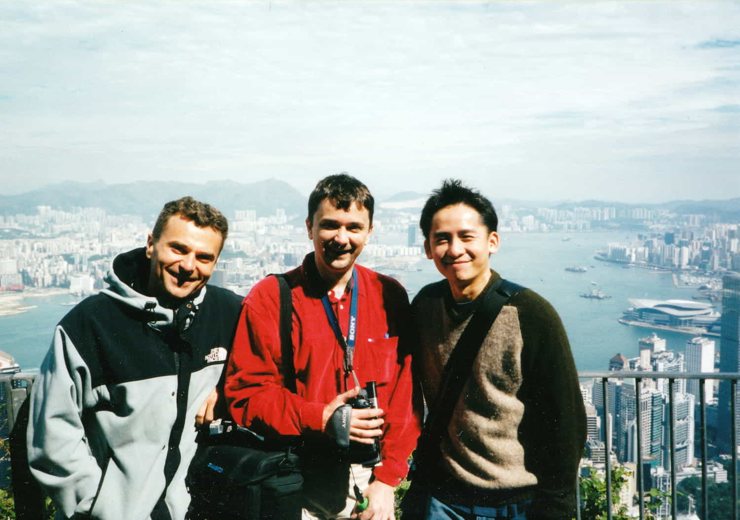 three people posing on a platform above a big city