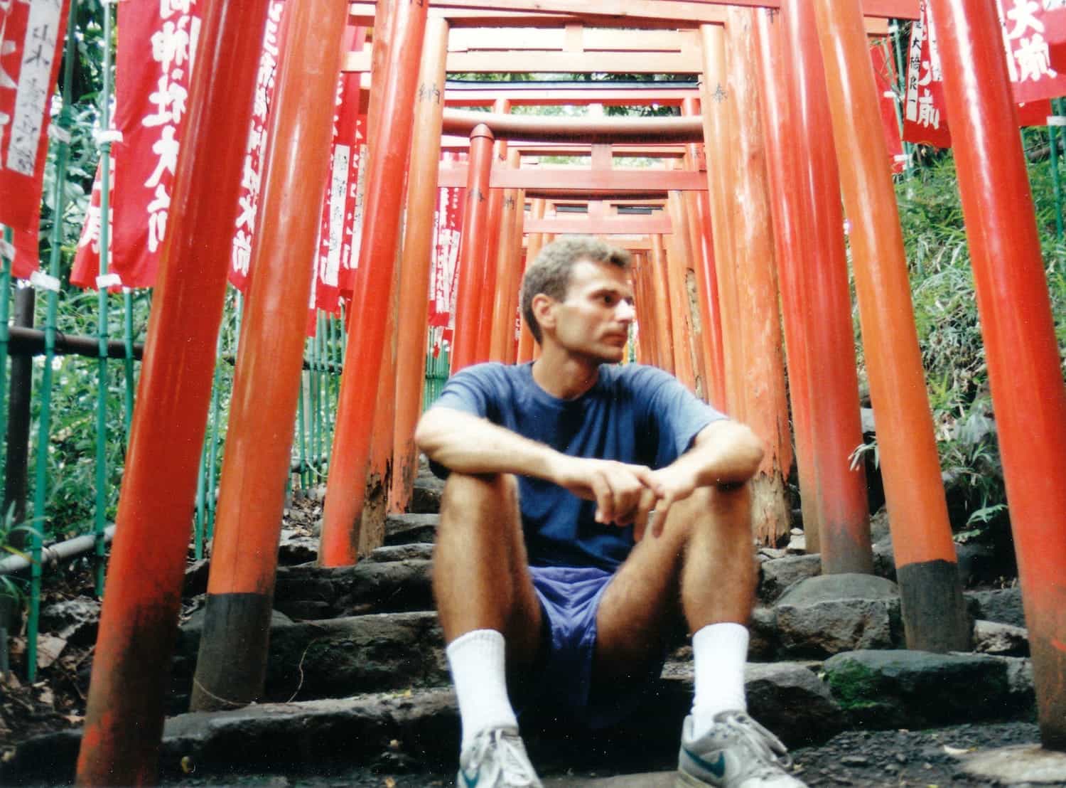 person sitting on steps under a series of red gates