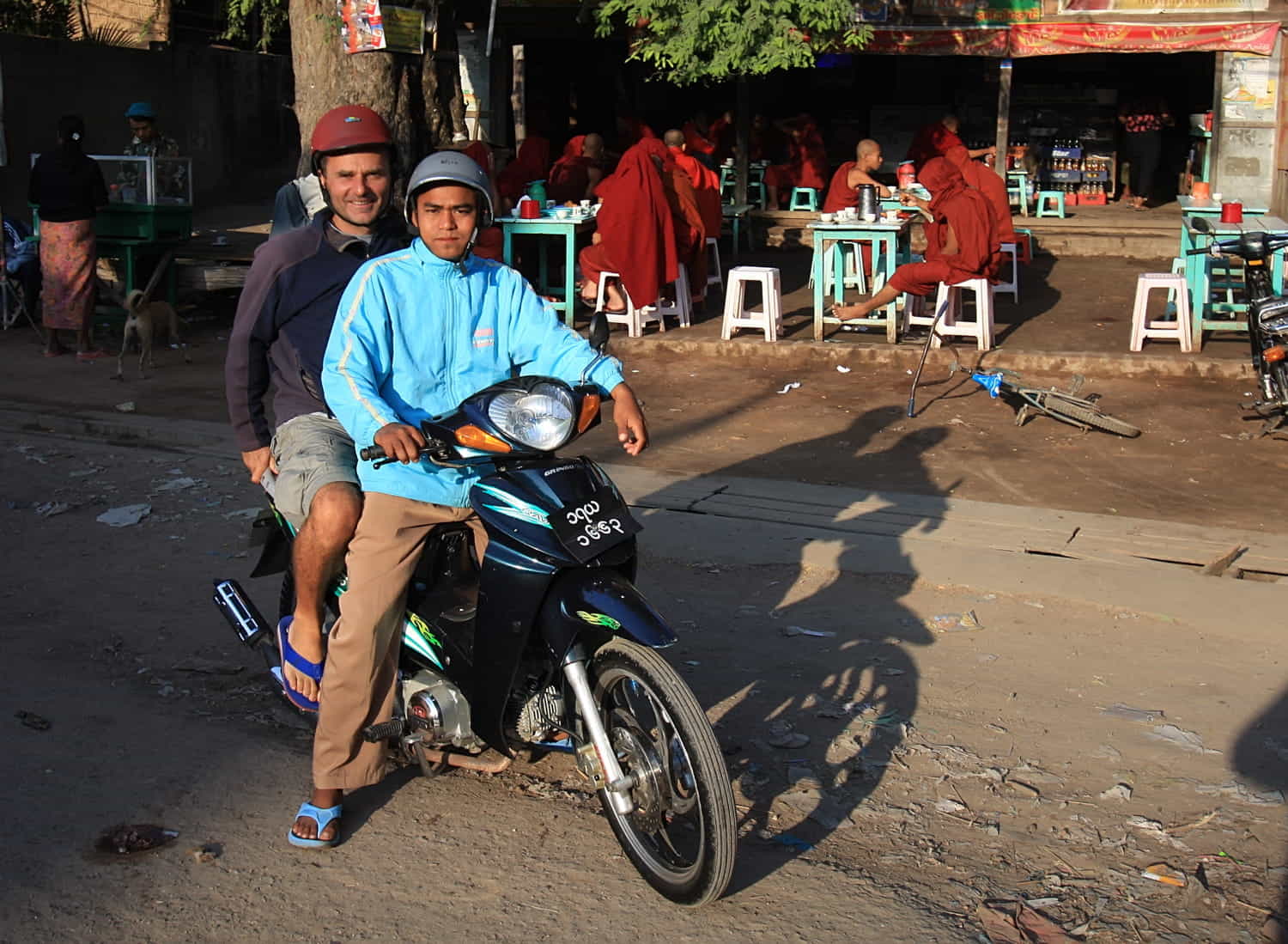 two guys on a scooter in front of a restaurant full of monks