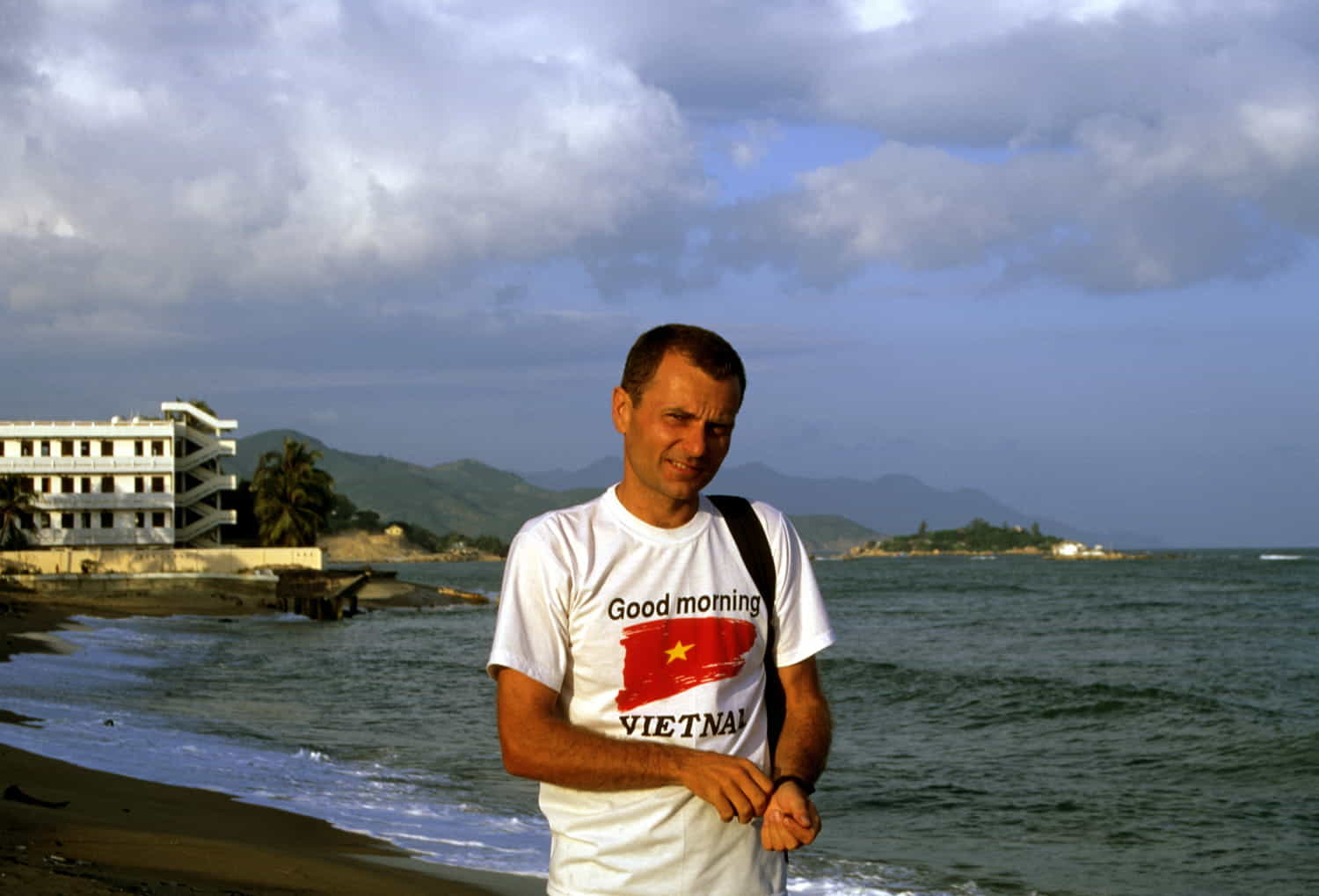 person wearing good morning Vietnam shirt next to a beach