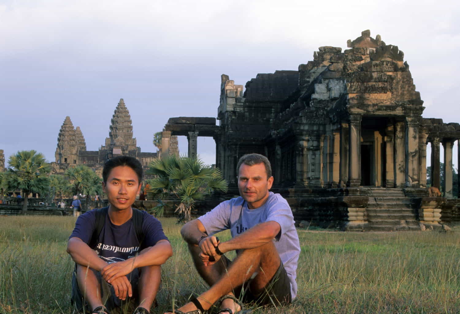 two people sitting on grassy field with Angkor wat temple behind