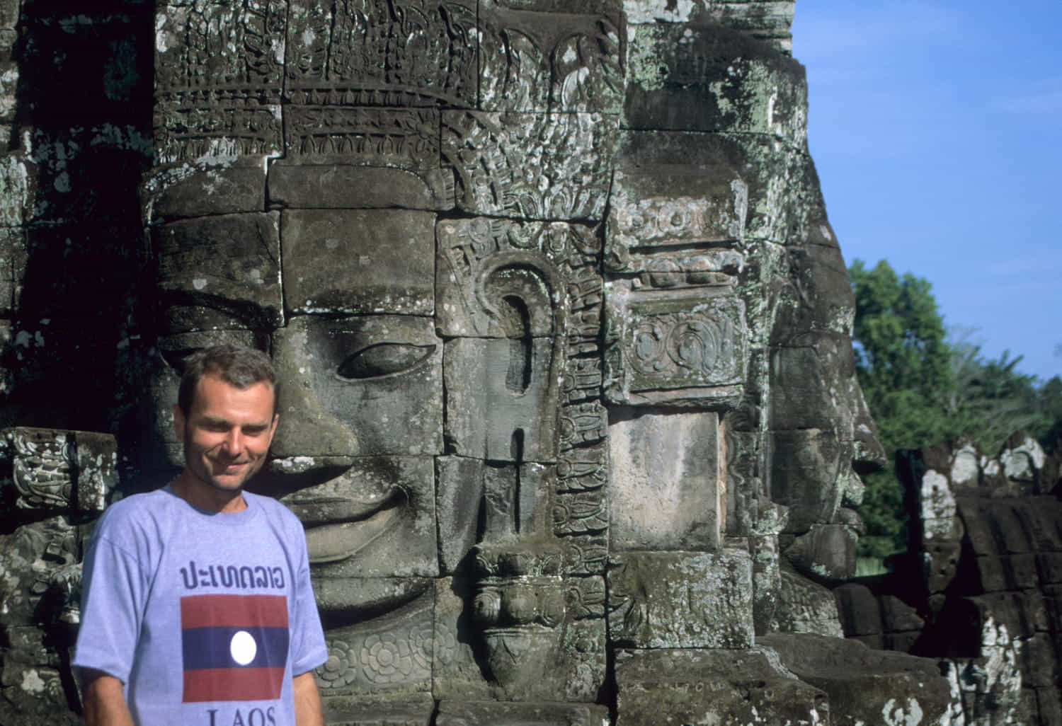 a person posing next to giant face carved in rock blocks