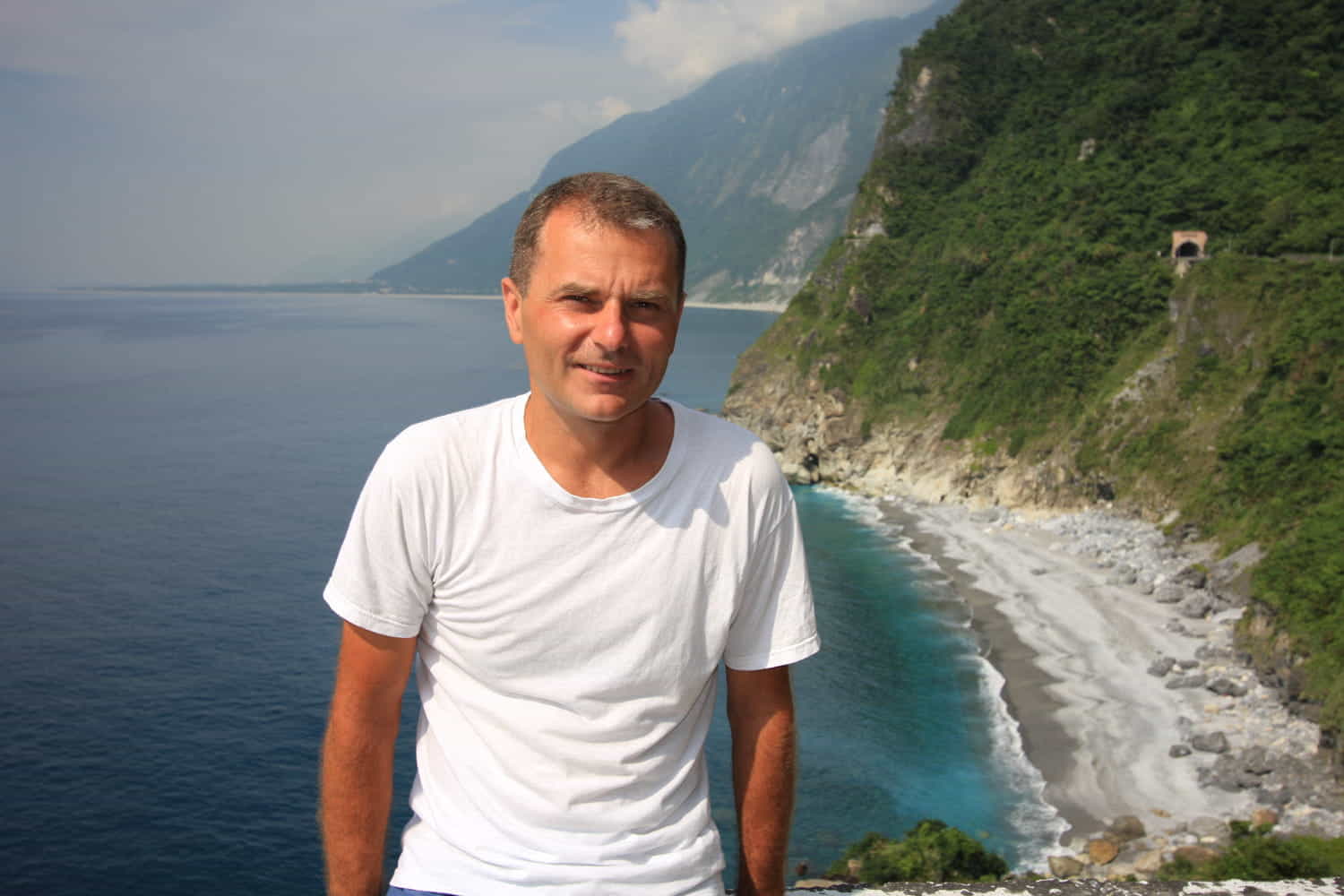 person posing high above the ocean with steep mountains descending into it