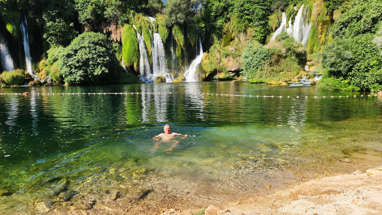 person swimming in a lake with waterfall behind