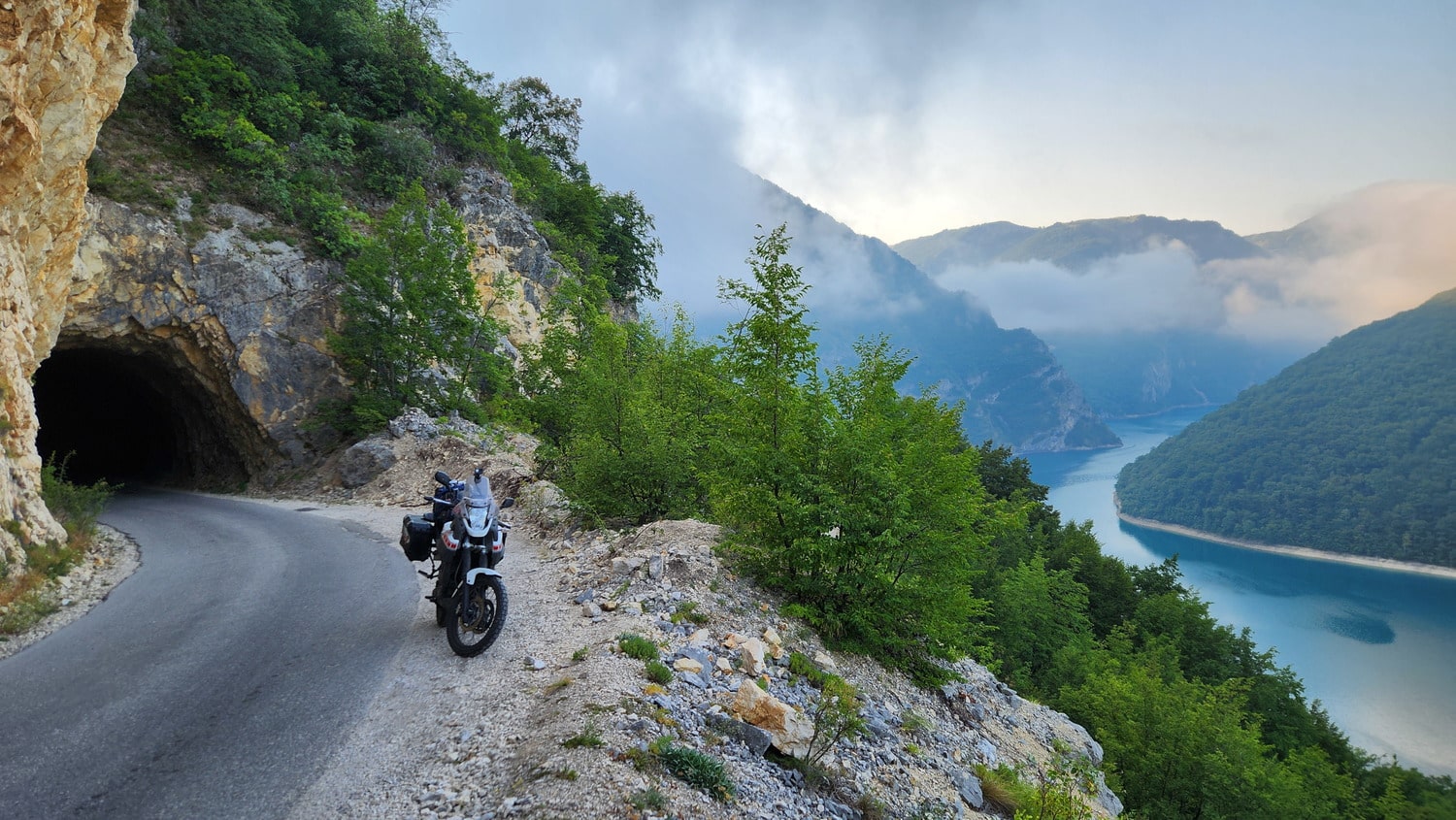 a motorcycle next to a tunnel, high above a lake