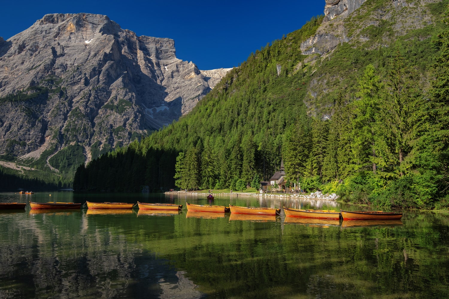 linked yellow boats on a green lake with high mountains behind