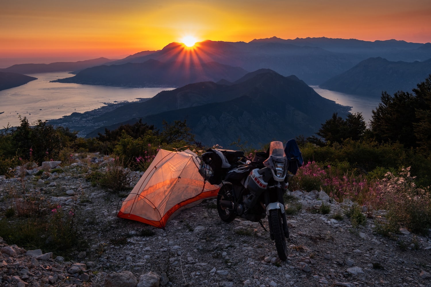 motorcycle and a tent high above a bay at sunset