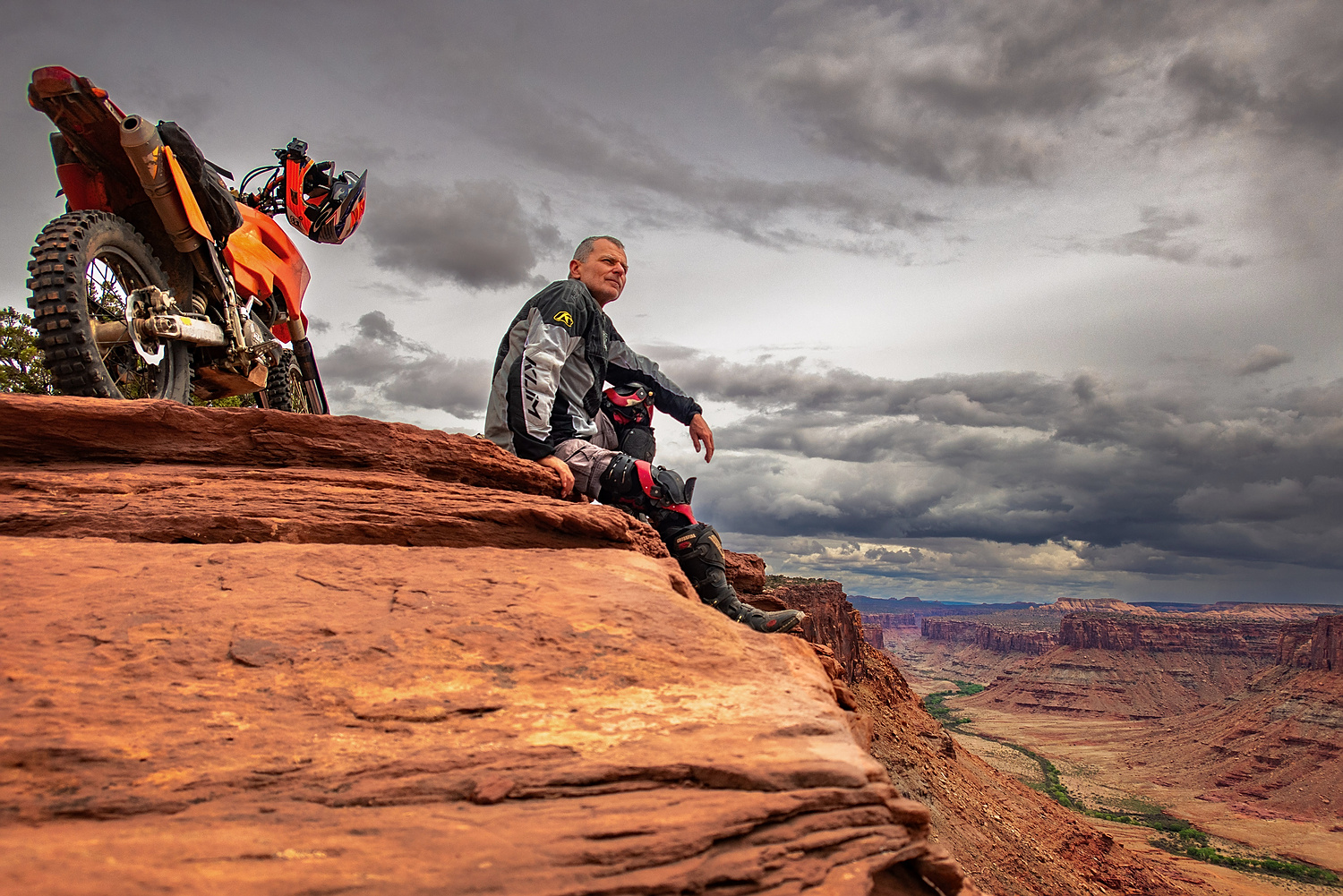 person sitting next to a motorcycle at the edge of a canyon