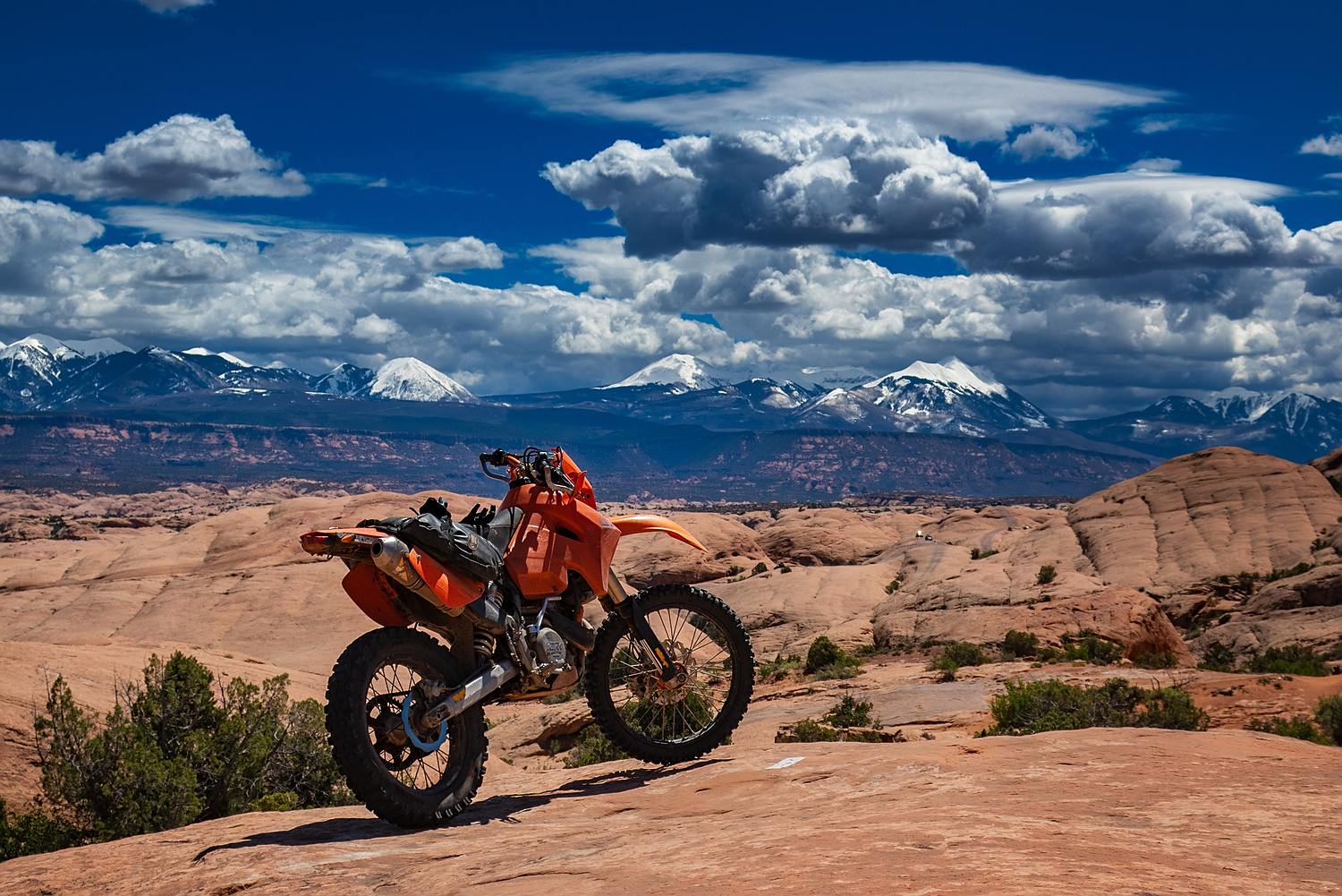 motorcycle parked on slick rock with snowy mountains behind