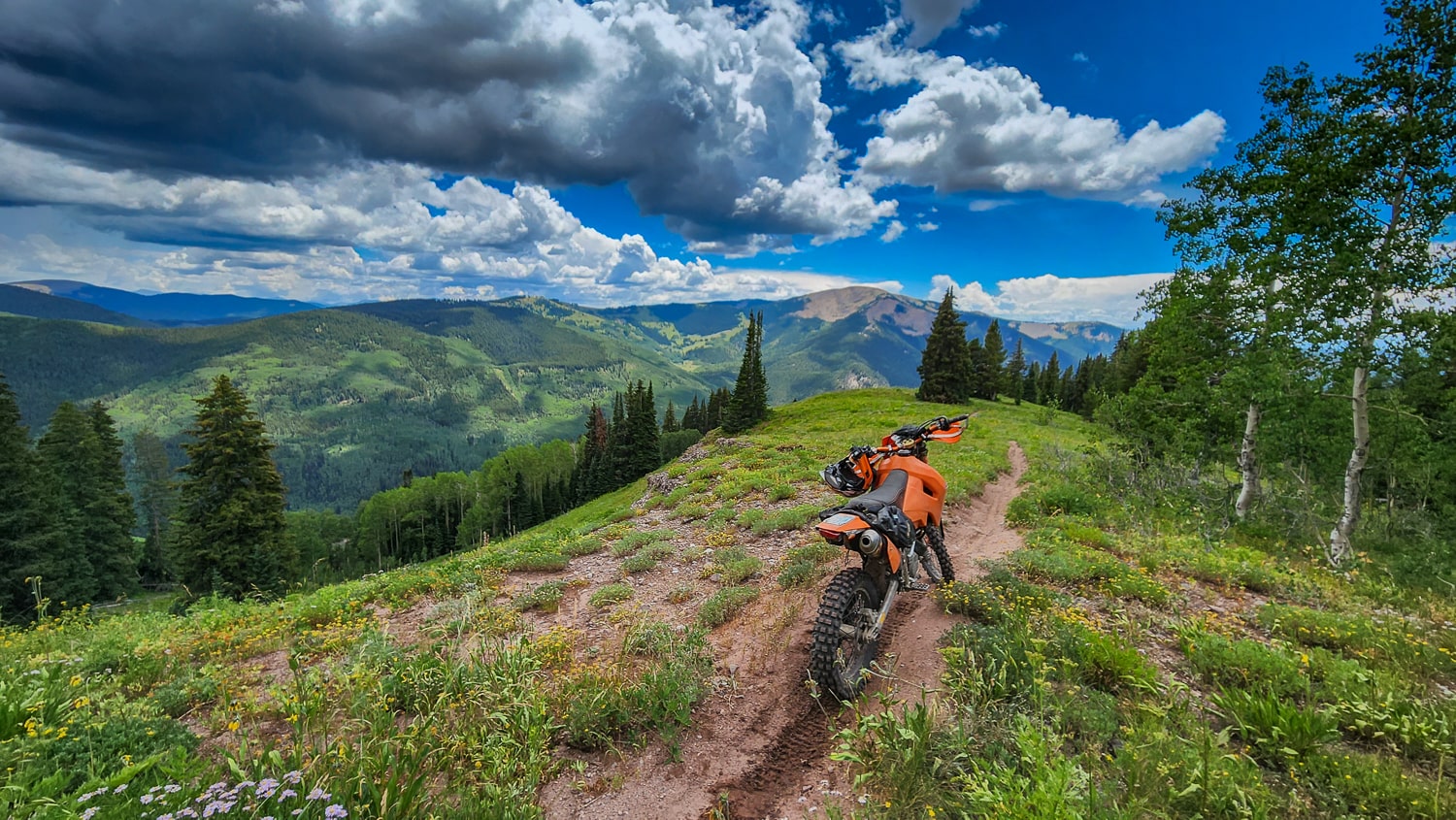 a motorcycle on trail cutting through grassy ridge with mountains behind