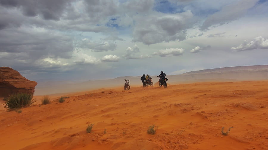 riders next to motorcycles with wind blown sand around them