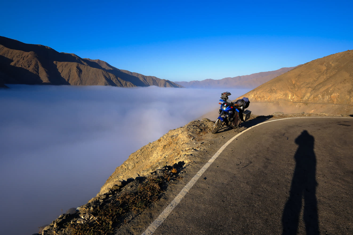 Motorcycle parked on a road with the valley below covered by clouds