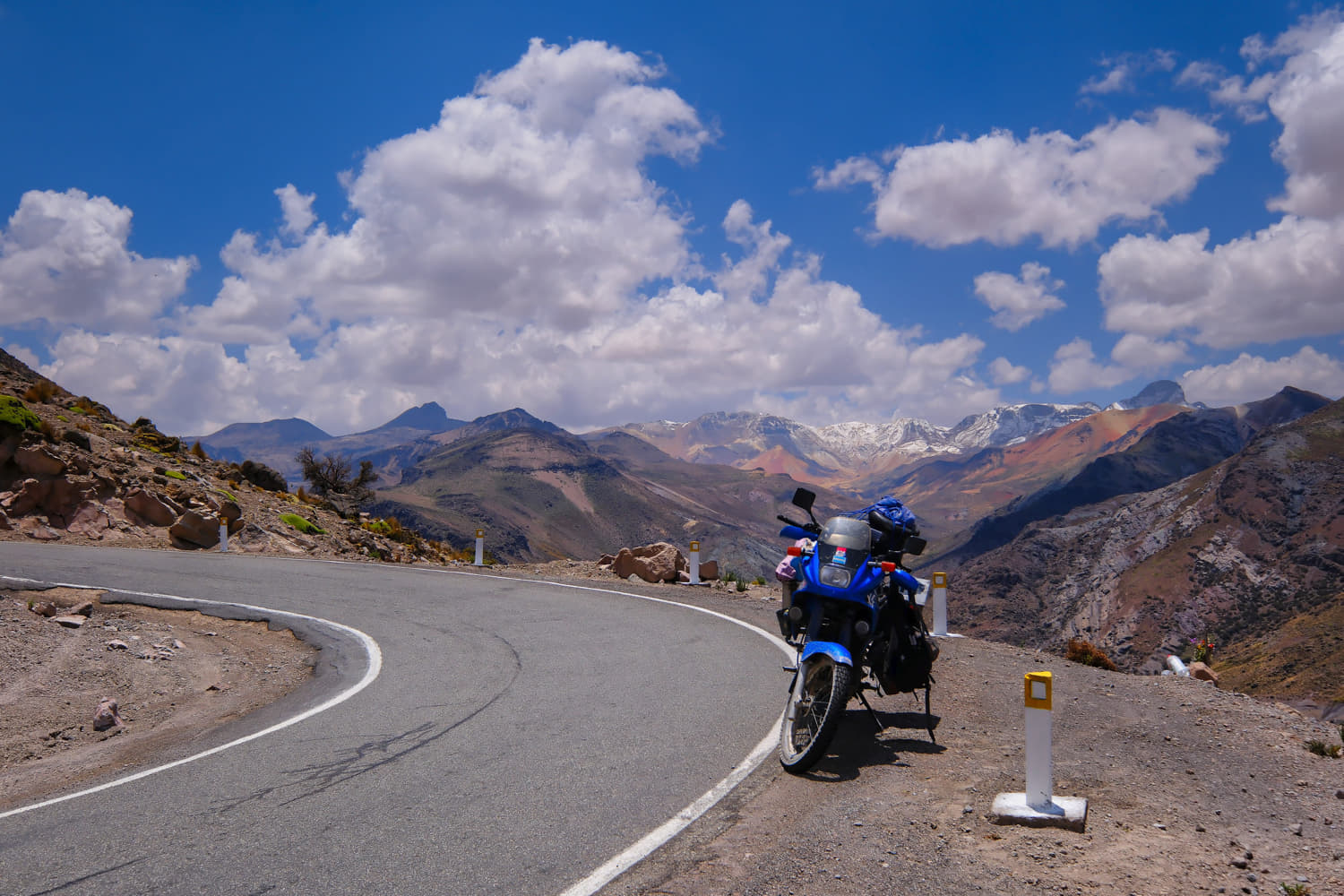 motorcycle parked on a desert road with snow covered 
             mountains behind