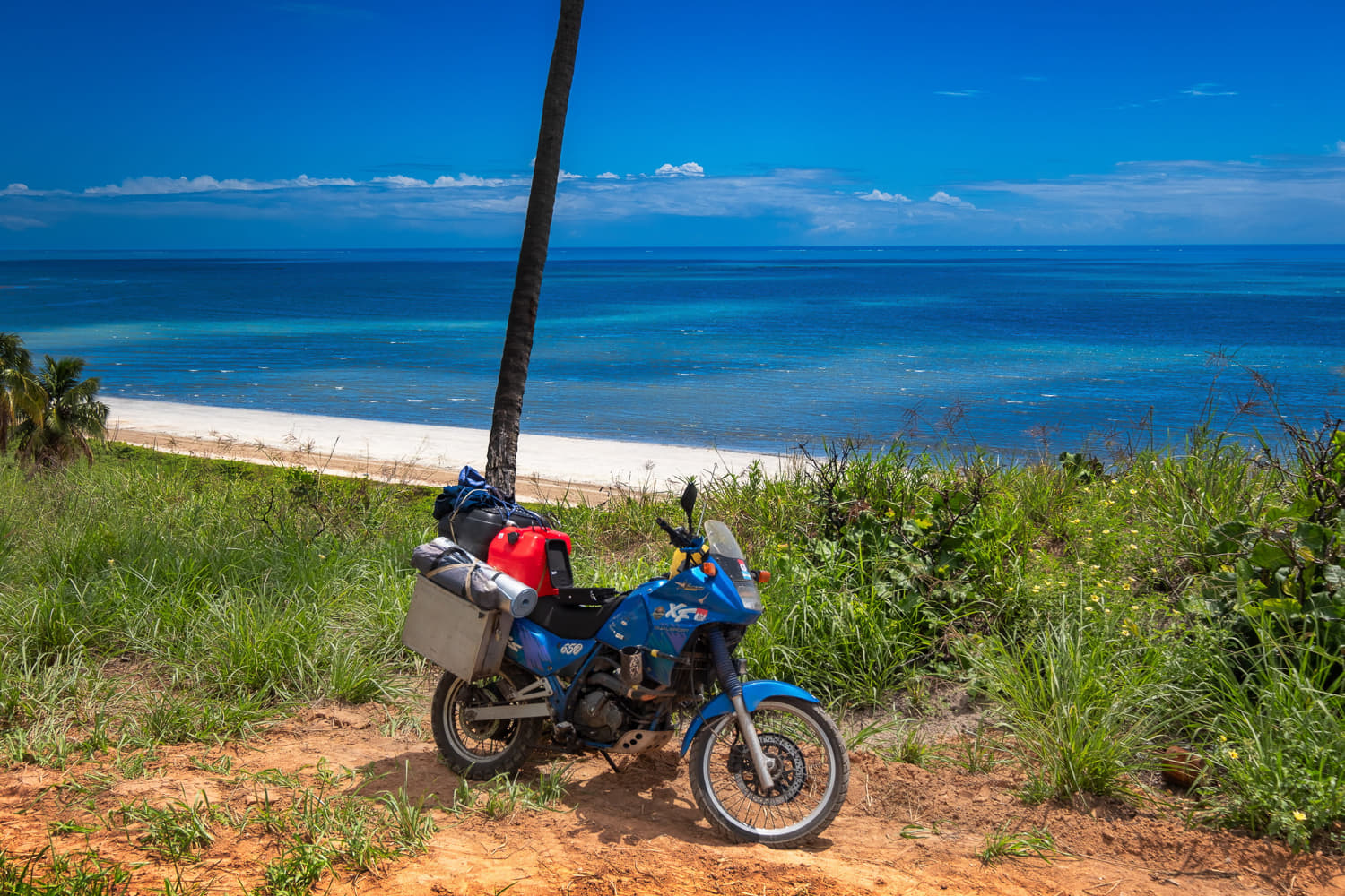 motorcycle parked high above a white sand beach and deep blue ocean