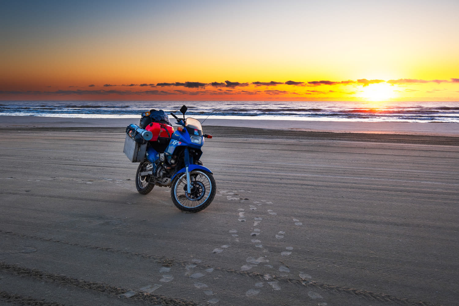 motorcycle parked on a beach with sun rising behind