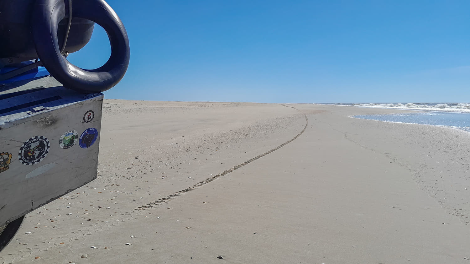 rear of a motorcycle panier and motorcycle wheel track on a vast empty beach