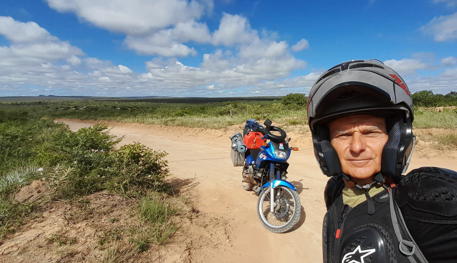 a selfie on a dirt track with motorcycle behind