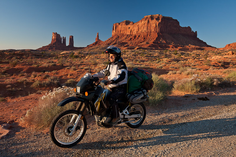 rider on a loaded bike with red rock spires behind
