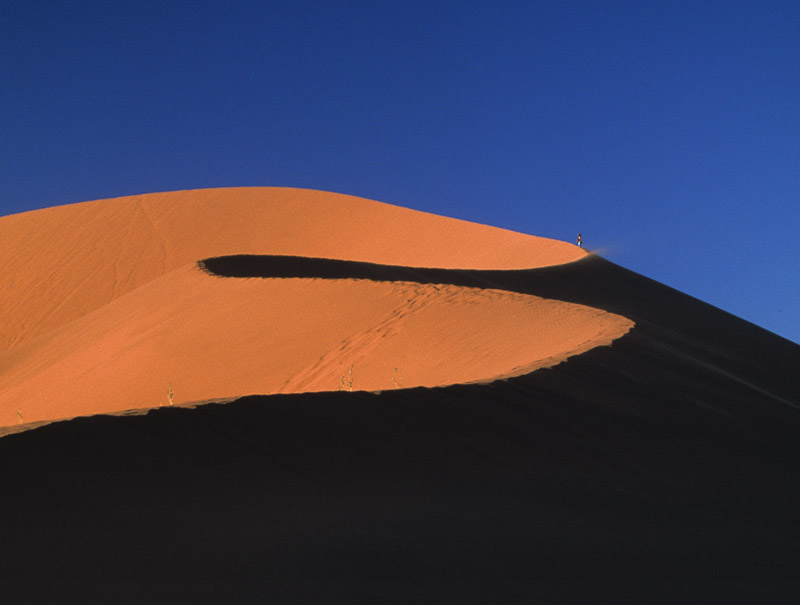 giant sand dune illuminated by setting sun, one side being dark