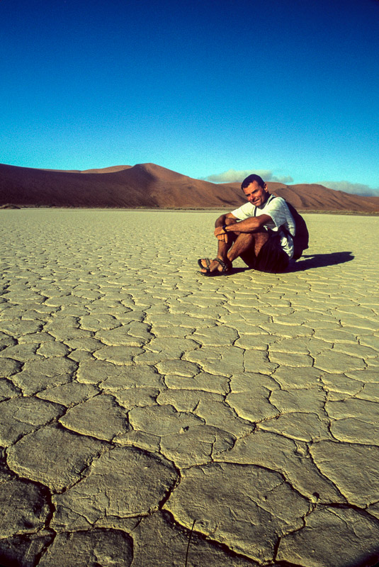 sitting on a dry lake bed with sand dunes behind