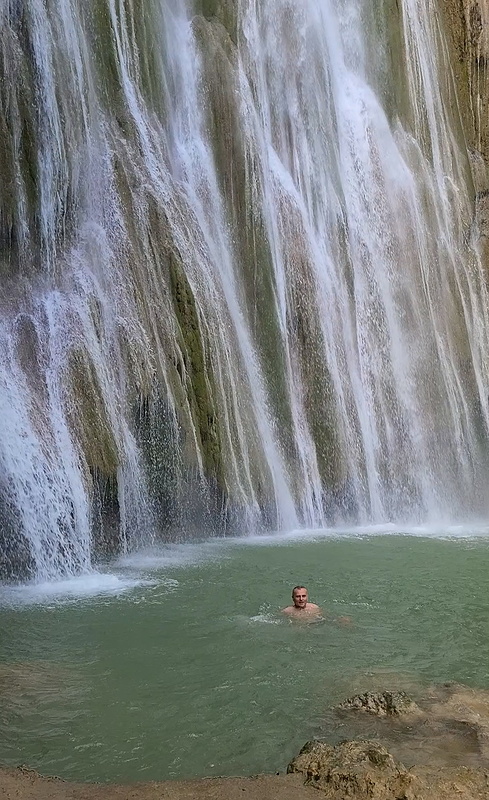 a person swimming in a pond at the base of a waterfall