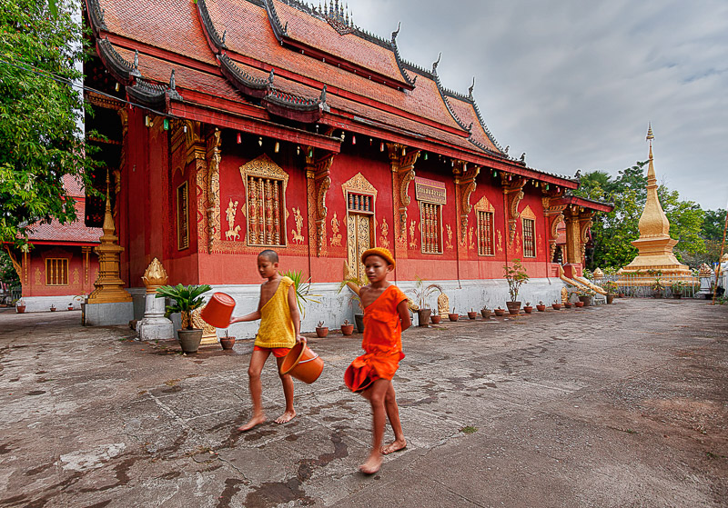 Two kids carrying buckets of water in front of red temple