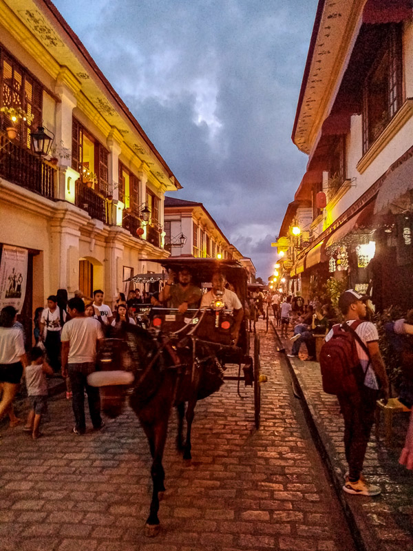 Crowded pedestrian street with horse carriages