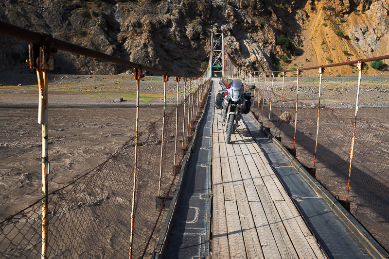 motorcycle parked on a narrow suspension bridge across raging river
