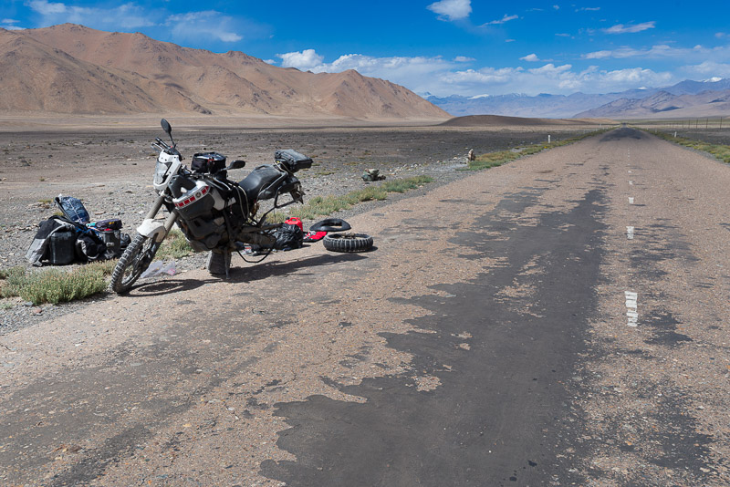 motorcycle parked on a desolate road with read wheel off for repair