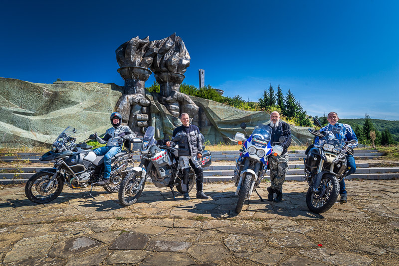 four riders with motorcycles in front of an imposing monument