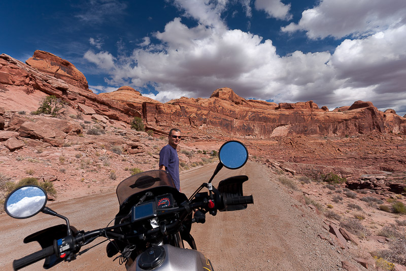 rider standing in front of a motorcycle with red vertical cliffs behind