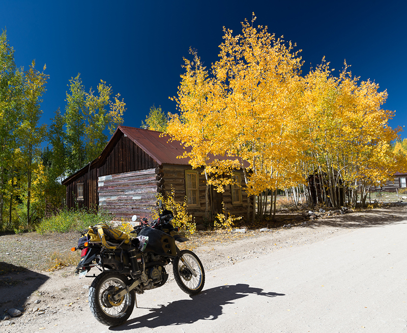 motorcycle next to an old wooden cabin and bright yellow aspen