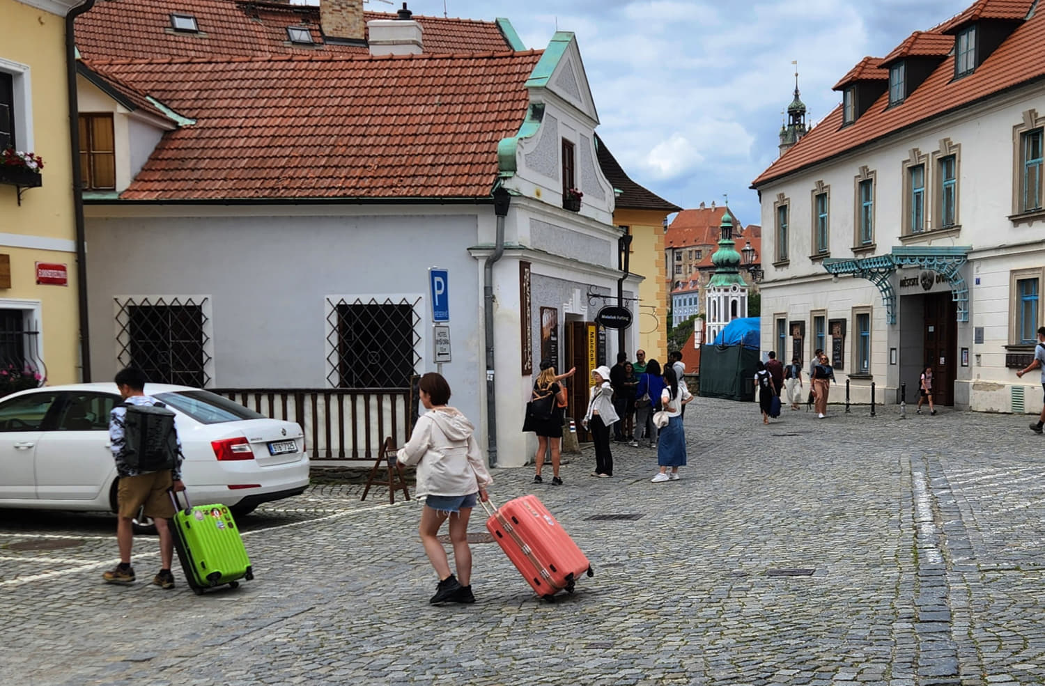 two people lugging suitcases on wheel on cobblestone street