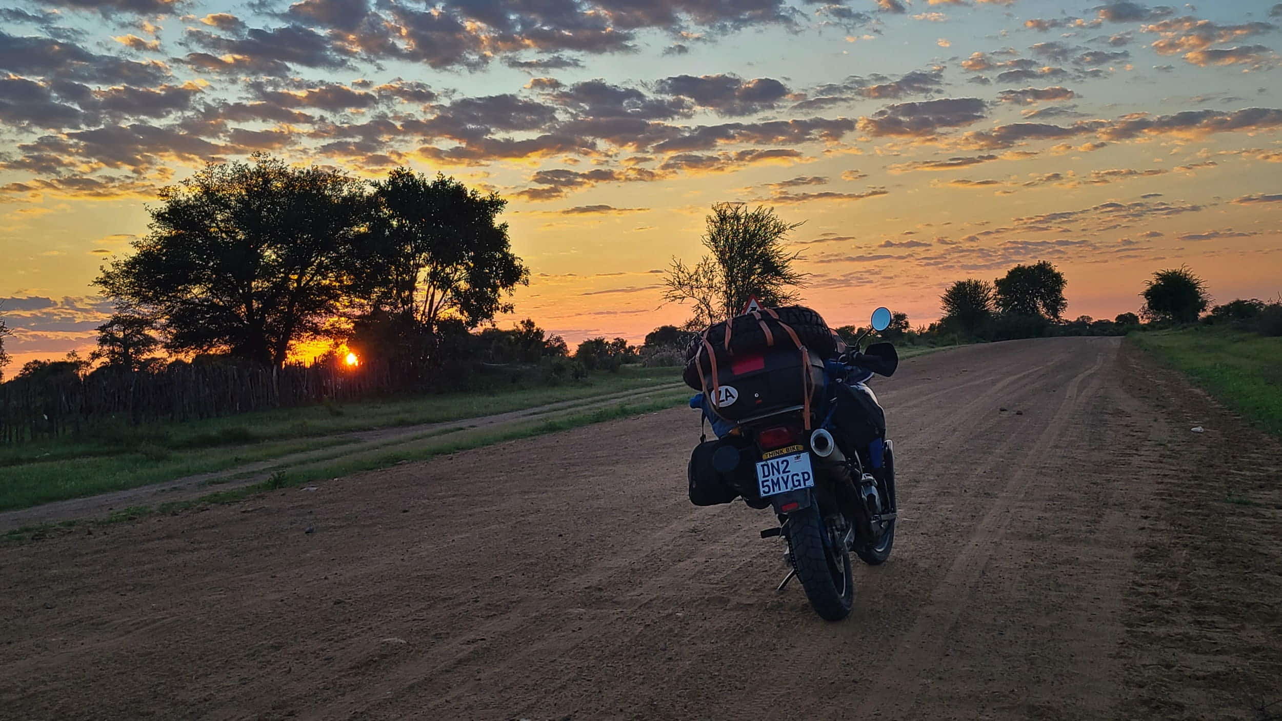 motorcycle parked on dirt road with sun peaking through threes