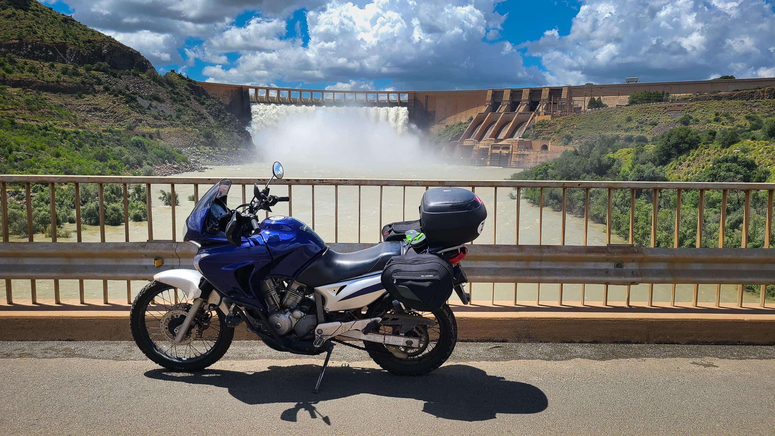 motorcycle parked on a bridge with overflowind dam behind 