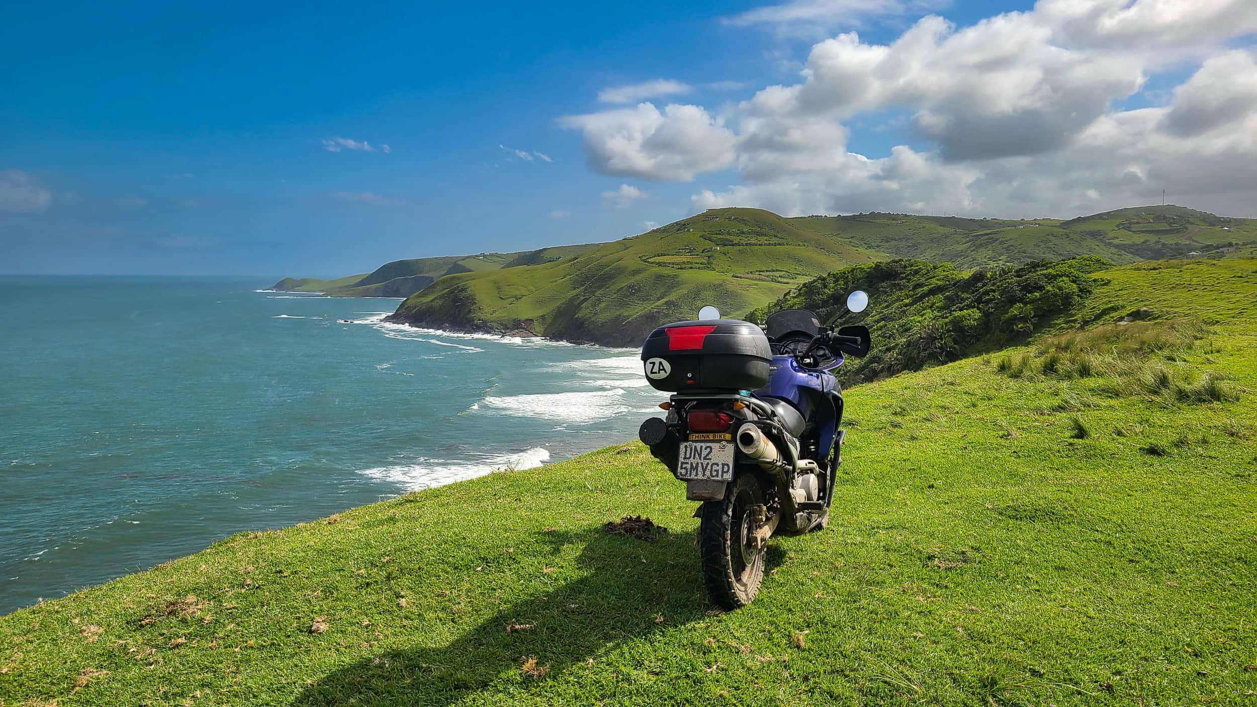 a motorcycle parked on green grass high above the ocean 