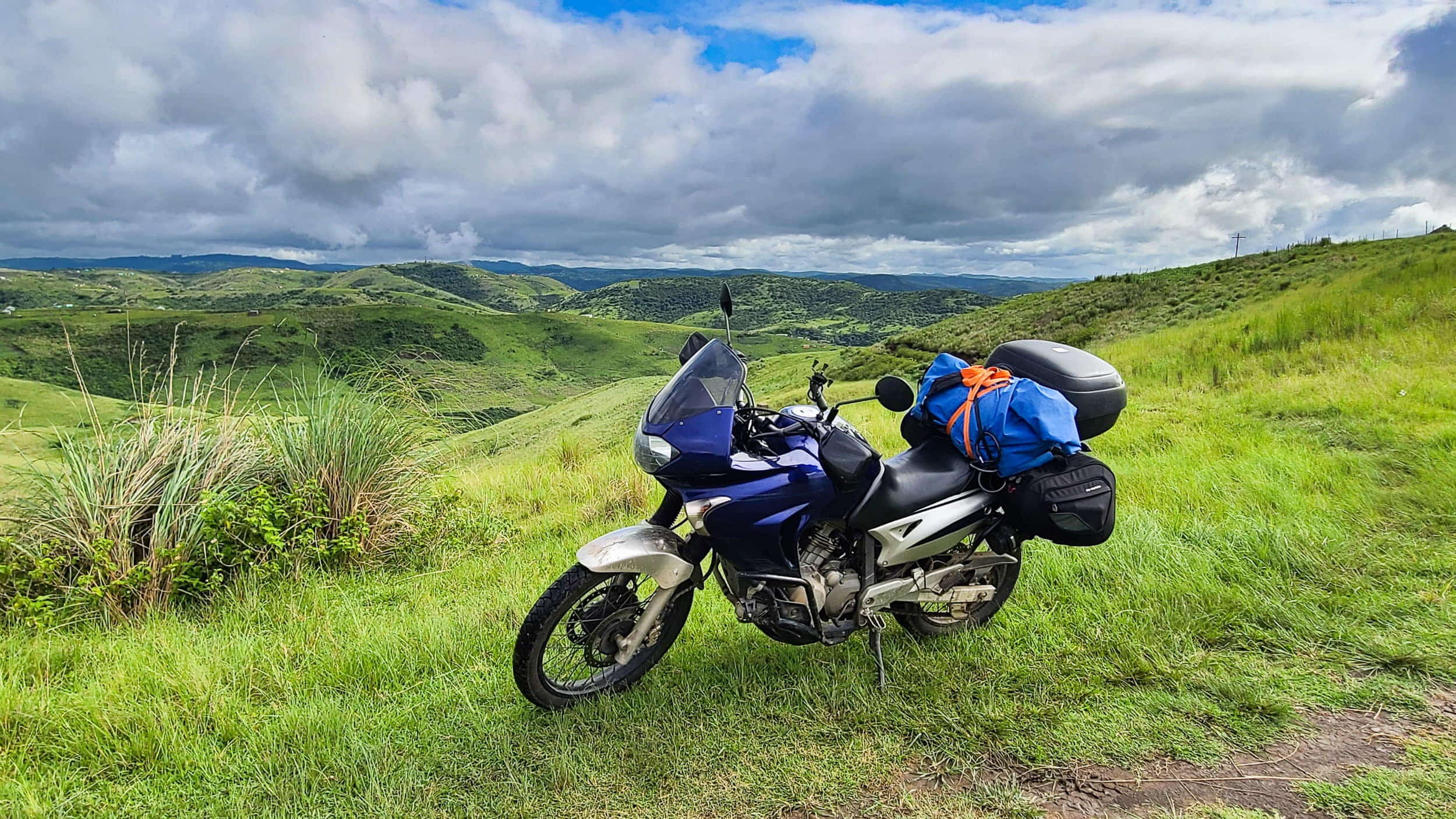 motorcycle parked on a road with green rolling hills behind