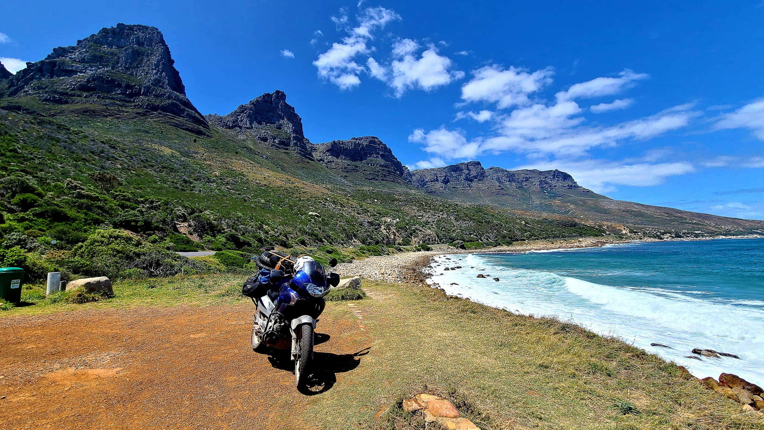 motorcycle parked with steep mountains descending into a blue ocean