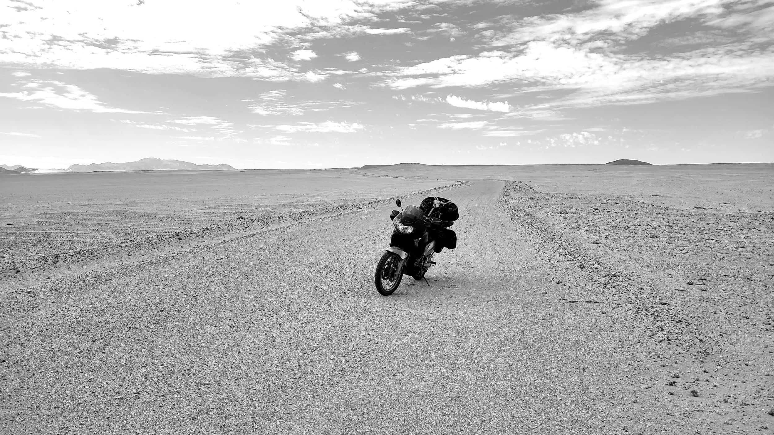 black and white photo of a motorcycle parked on a desolate gravel road