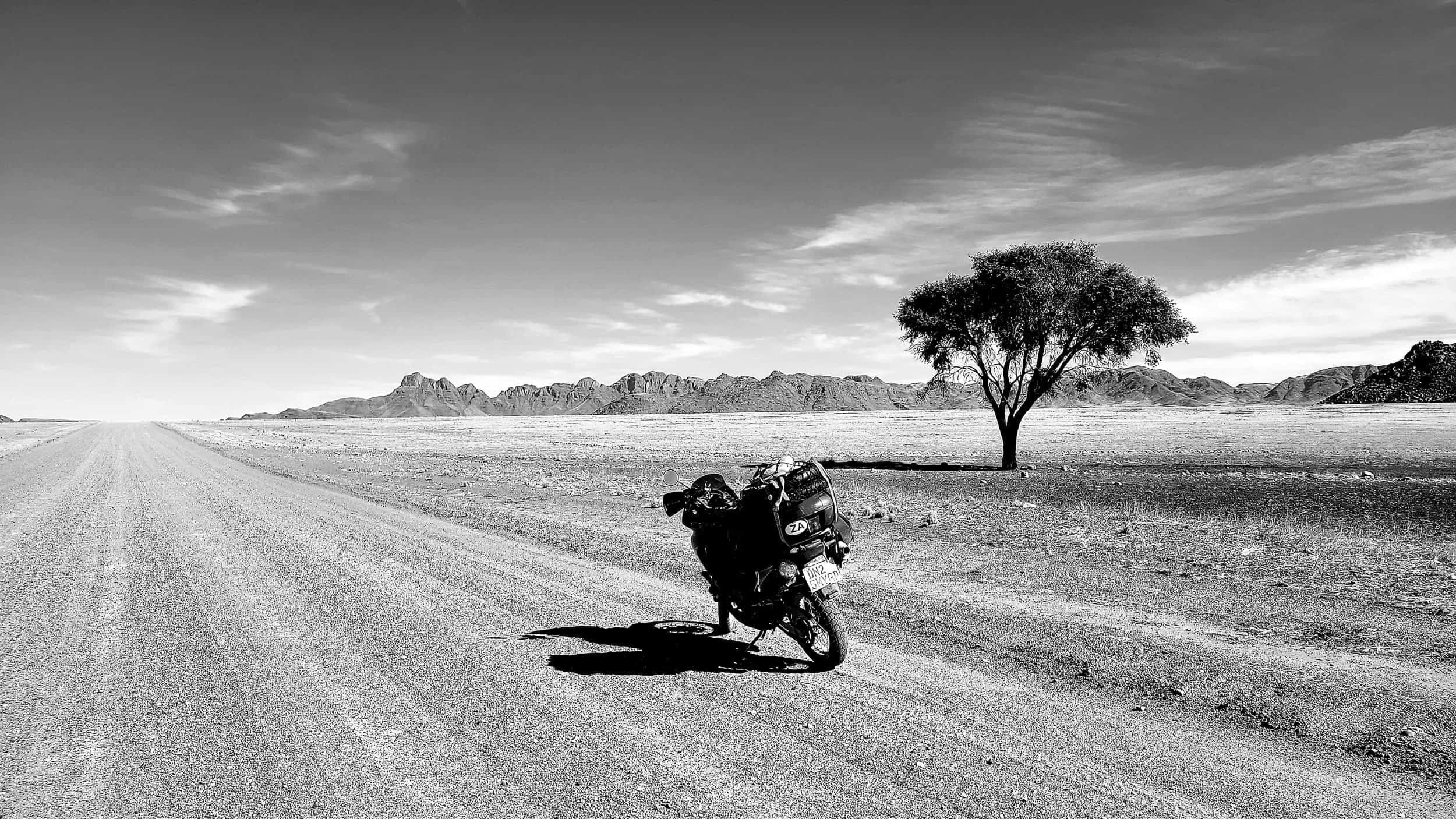 black and white photo of a motorcycle and a lone tree in desert